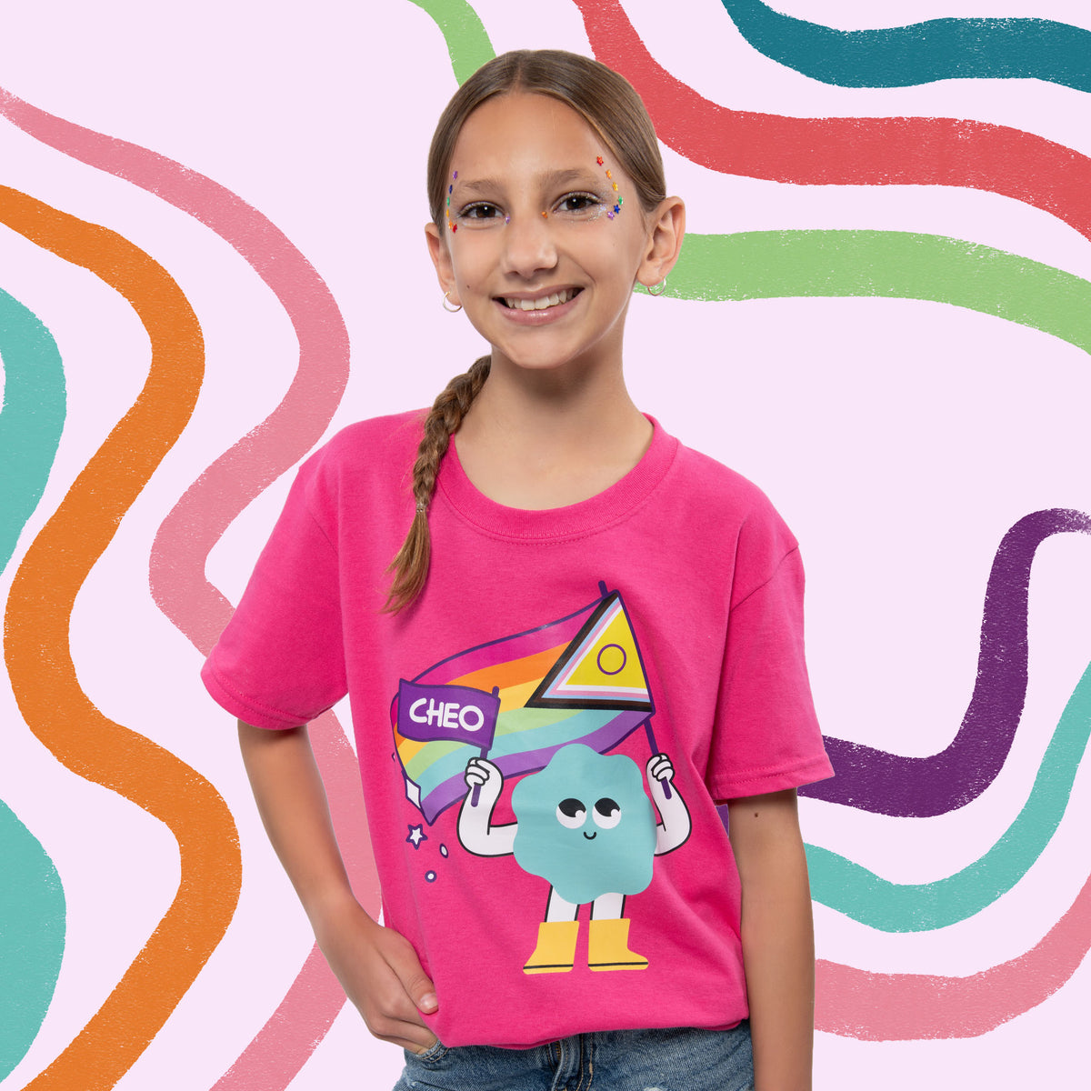 A young girl with a braided ponytail smiles while wearing a bright pink t-shirt with a colorful cartoon graphic of a blue cloud character holding a rainbow flag. The background is a playful, abstract wavy pattern in pastel pink, teal, orange, green, and purple.